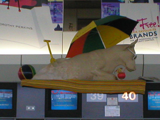 A sand-castle cow, with spade, beach ball, umbrella and sunglasses, lying on the monitors above a check in desk