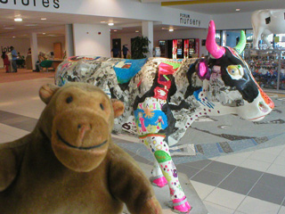 Mr Monkey in front of a cow decorated in a mix of black, bright colours and photos