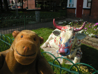 Mr Monkey in front of a reclining cow covered in bright pictures by children the guise of a shoe