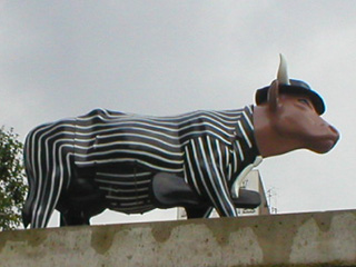 A cow in a pin-striped suit and fedora, carrying a violin case