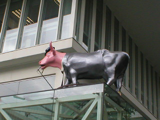 A cow in a silver-grey suit and pork pie hat, with microphone stand 