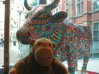 Mr Monkey in front of a cow covered in rows of acrylic gems