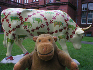 Mr Monkey in front of a pale yellow cow decoated with small patterned cows and borders