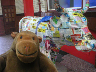 Mr Monkey with a cow covered in colourful tickets and flyers
