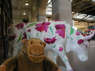 Mr Monkey in front of a cow decorated with large purple flowers