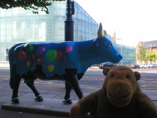 Mr Monkey with a cow decorated with balloons flying above a city skyline