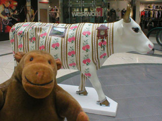 Mr Monkey in front of a cow decorated with a wallpaper pattern