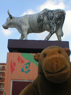 Mr Monkey looking up at a black and white cow