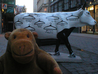Mr Monkey in front of a cow painted with coat hangers