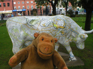 Mr Monkey in front of a map covered cow