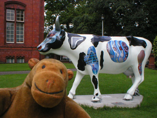 Mr Monkey in front of a cow with patches of skin missing to show mechanical internal workings
