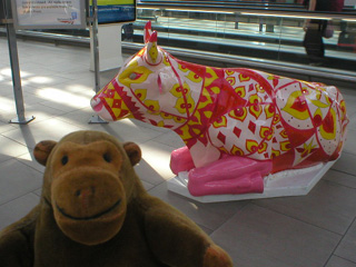 Mr Monkey in front of a reclining cow patterned with bands of pink and yellow