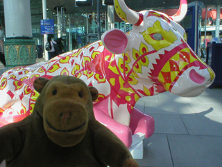 Mr Monkey in front of a reclining cow patterned with bands of pink and yellow