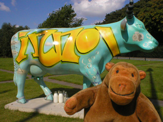 Mr Monkey in front of a turquoise cow with yellowing writing on it