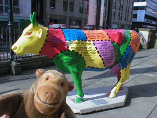 Mr Monkey in front of a cow decorated with patches of bright colours