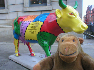 Mr Monkey in front of a cow decorated with patches of bright colours