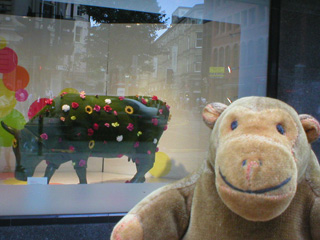 Mr Monkey looking at a green cow in a shop window