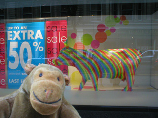 Mr Monkey looking at a rainbow striped cow in Kendals' window
