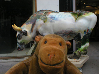 Mr Monkey in front of a cow representing the Lake District