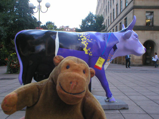 Mr Monkey in front of a cow in a purple and black uniform