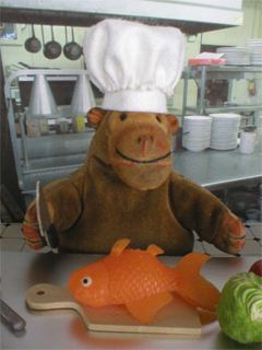 Mr Monkey wearing his chef's toque while cutting up a fish in a modern restaurant kitchen
