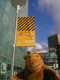 Mr Monkey looking at a Haçienda exhibition banner outside Urbis