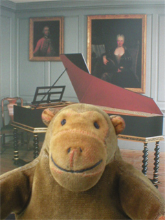 Mr Monkey in front of a photo of a replica harpsichord