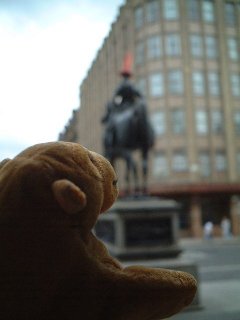 Mr Monkey looking at a statue with a traffic cone on its head