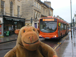 Mr Monkey looking at a bright orange Bath bus