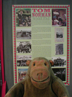 Mr Monkey reading an information panel about Tom Norman