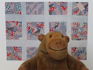 Mr Monkey in front of a postcard of a wartime quilt