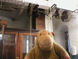 Mr Monkey looking up at the old power train for winding the clock