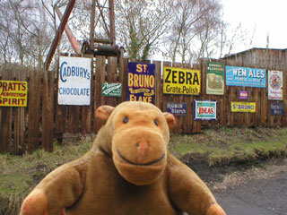 Mr Monkey with a fence covered in adverts