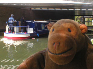 A narrowboat goes under a bridge as Mr Monkey walks along the canal