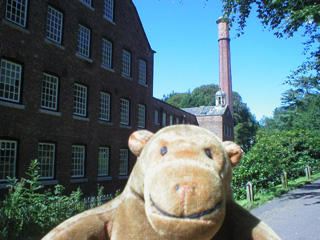 Mr Monkey looking at a factory with many windows and a high chimney