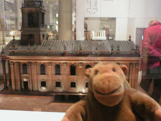 Mr Monkey in front of a wooden model of a church