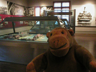 Mr Monkey in front of a model of Ellis Island