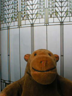 Mr Monkey in front of a picture of a Frank Lloyd Wright window
