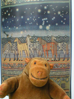 Mr Monkey in front of a picture of a Swedish wallhanging