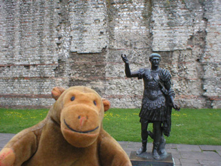 Mr Monkey in front a Roman wall and a statue of Trajan