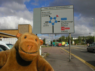 Mr Monkey in front of the Magic Roundabout roadsign
