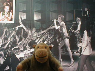 Mr Monkey in front of a picture of a Bowie concert