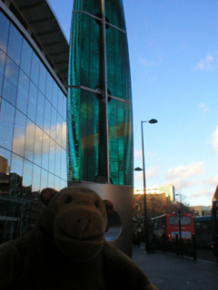 Mr Monkey at a green glass column outside The Gate