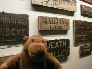 Mr Monkey in front of a display of trench nameboards, including Martin's Lane and Death Valley
