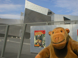 Mr Monkey looking at exhibition posters on the fence outside the IWM North
