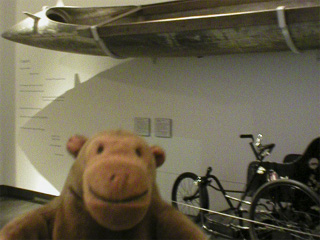 Mr Monkey looking at a canoe and an invalid carriage in Silo 6