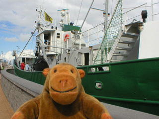 Mr Monkey walking past a trawler in a dry dock
